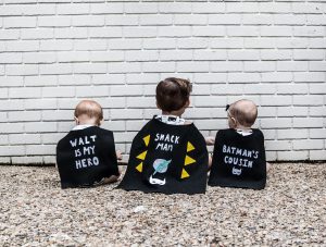 Batman kids' birthday party decor; toddler and babies in capes facing a brick wall